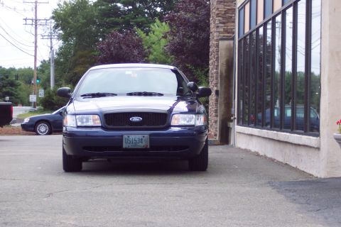 2001 Ford Crown Victoria - A dark blue 2003 Ford Crown Victoria police car is parked in front of a building with large windows, with another vehicle visible in the ba…