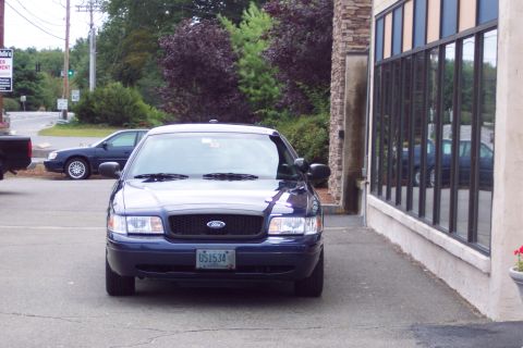 2001 Ford Crown Victoria - A dark blue 2001 Ford Crown Victoria is parked in front of a building with large windows. Another car is visible in the background.