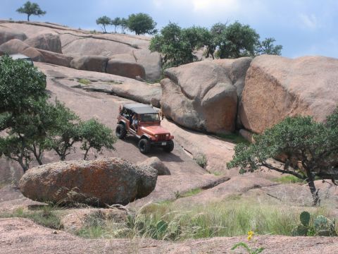 2001 Jeep Wrangler - An orange Jeep Wrangler navigates a steep, rocky incline, with another vehicle visible in the distance.