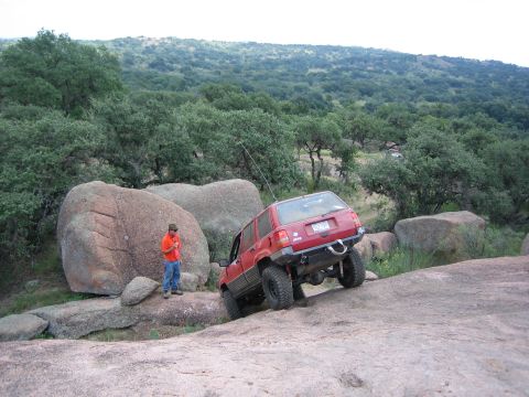 2001 Jeep Wrangler - Red Jeep Grand Cherokee navigating a rocky off-road course with a person observing.