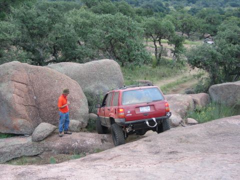 2001 Jeep Wrangler - A red Jeep Grand Cherokee is shown off-roading on a rocky trail, with a person observing its progress.