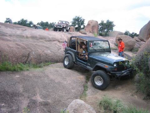 2001 Jeep Wrangler - A dark green Jeep Wrangler navigates a rocky trail, with another Jeep visible in the distance.