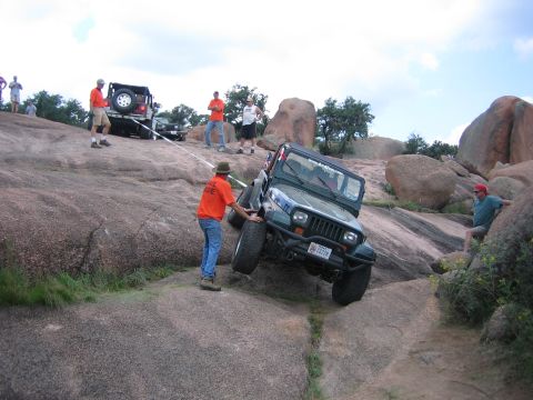 2001 Jeep Wrangler - A dark green Jeep Wrangler YJ with a tube front bumper, mud-terrain tires and a Texas plate climbs a steep granite slab while being winched…