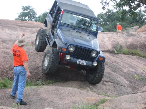 2001 Jeep Wrangler - A blue 2001 Jeep Wrangler navigates a challenging rocky terrain, guided by a person in an orange shirt.