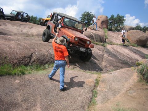 2001 Jeep Wrangler - A group of Jeeps navigates a challenging rocky terrain, guided by an orange-shirted attendant.