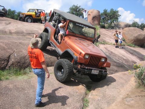 2001 Jeep Wrangler - An orange Jeep Wrangler tackles a challenging rocky trail, with a trail guide observing its progress.