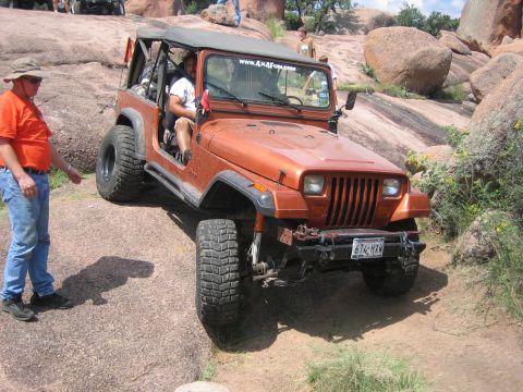 2001 Jeep Wrangler - An orange Jeep Wrangler navigates a rocky trail, with a person standing to the side and another person driving.