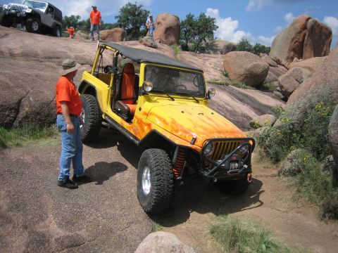 2001 Jeep Wrangler - A yellow Jeep Wrangler with flame decals navigates a rocky off-road trail with a man standing nearby.
