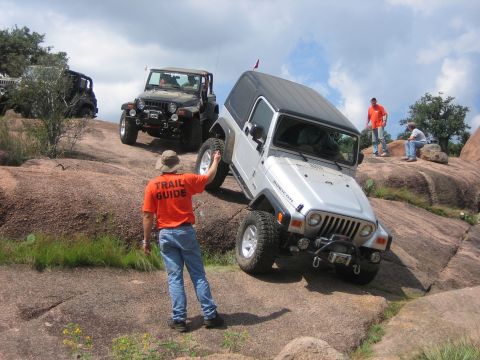 2001 Jeep Wrangler - Several Jeeps navigate a challenging rocky off-road course with a trail guide present.
