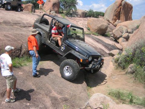 2001 Jeep Wrangler - A black Jeep Wrangler navigates a rocky off-road trail with spectators watching.