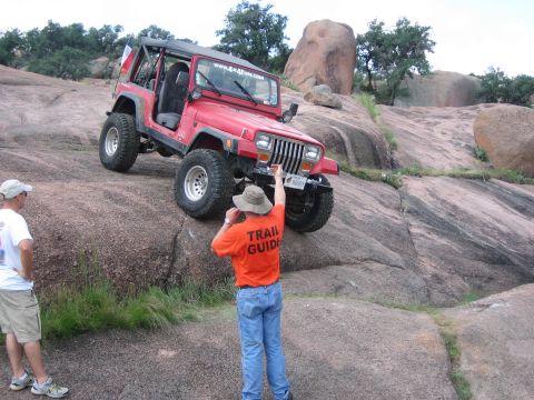 2001 Jeep Wrangler - A red Jeep Wrangler navigates a steep, rocky incline with two people observing the climb.