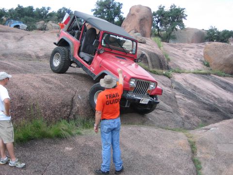 2001 Jeep Wrangler - A red Jeep Wrangler navigates a steep, rocky incline with a trail guide offering direction.