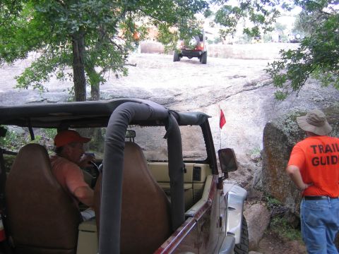 2001 Jeep Wrangler - A maroon Jeep Wrangler, driven by a man in an orange cap, maneuvers through a rocky trail while a trail guide watches.