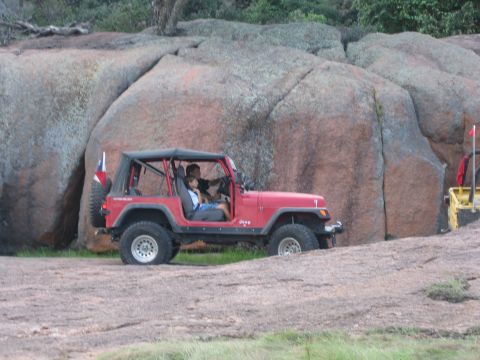 2001 Jeep Wrangler - A red Jeep Wrangler navigates a rocky landscape, with two occupants visible inside the vehicle.