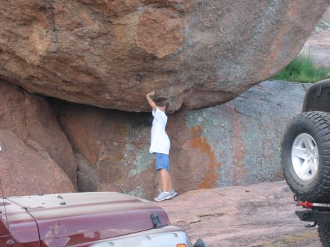 2001 Jeep Wrangler - A young person stands beneath a massive rock formation, with two Jeep vehicles nearby.