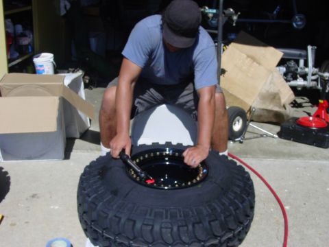 1994 Ford Bronco - Person working on a large off-road tire and wheel assembly.
