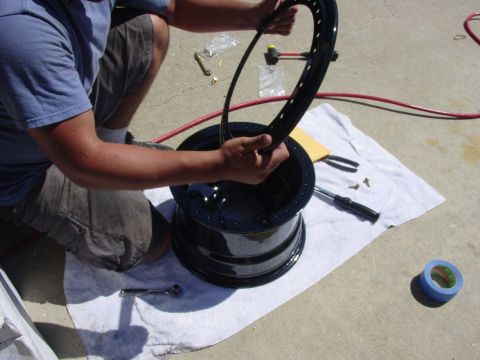 1994 Ford Bronco - A person is working on a black wheel rim, likely during tire installation or repair.
