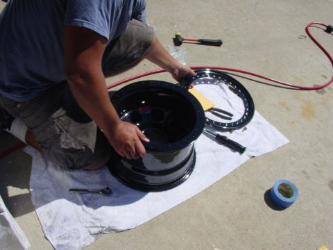 1994 Ford Bronco - A person is working on a black wheel rim, with tools like a torque wrench and a hammer nearby.