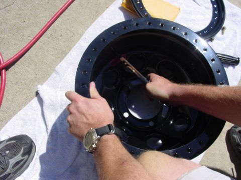 1994 Ford Bronco - Cleaning a black wheel rim with a brush, with a red hose nearby.