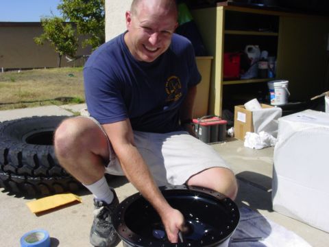 1994 Ford Bronco - A man cleans a car wheel outdoors, with a large tire and car battery visible in the background.