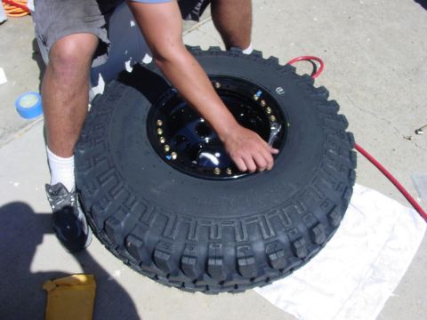 1994 Ford Bronco - A person is working on a tire and wheel assembly, tightening lug nuts with a wrench.