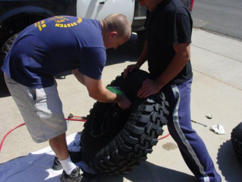 1994 Ford Bronco - Two men are working on a large off-road tire next to a white truck, possibly a Ford Bronco.