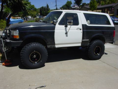 1994 Ford Bronco - Side view of a lifted black Ford Bronco in a driveway mid-repaint, with a white hardtop and a freshly white-painted driver's door contrasti…