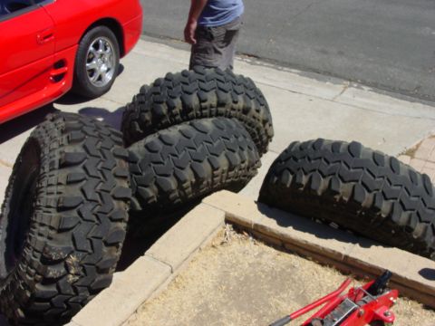 1994 Ford Bronco - A red sports car is partially visible next to a set of four large off-road tires laid out on the ground.