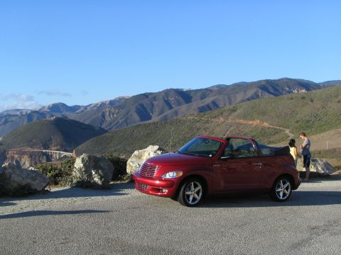 2005 Chrysler PT Cruiser - A red 2005 Chrysler PT Cruiser convertible is parked at a scenic overlook with mountains and a bridge visible in the distance.