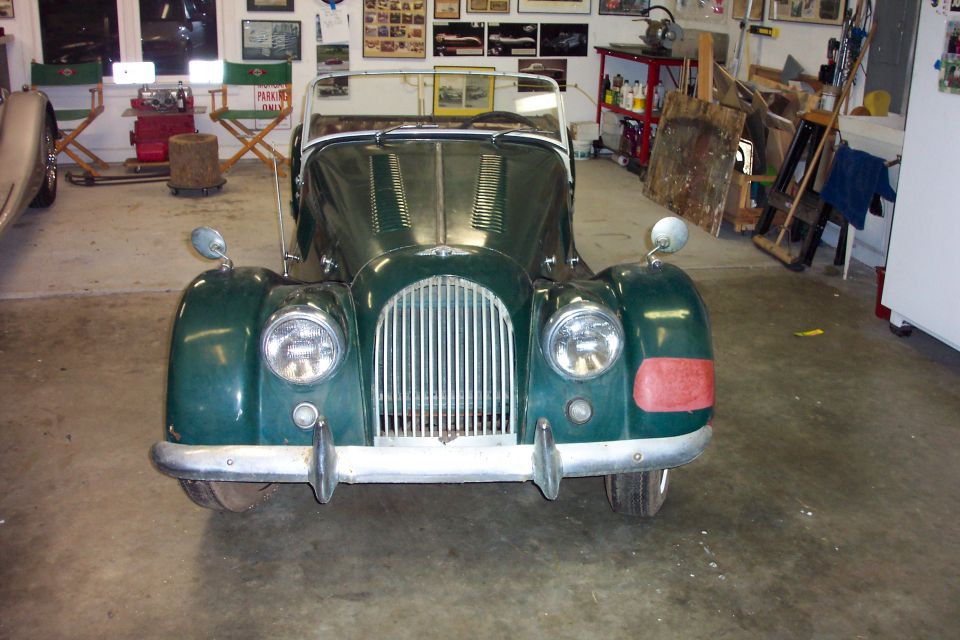 Dark green Morgan roadster head-on in a garage with red primer patch on the front fender