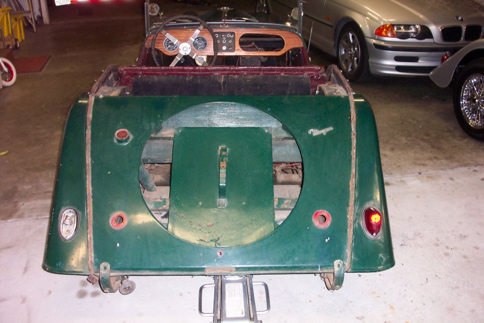 Rear of a green Morgan roadster in restoration, spare-wheel recess empty, wood dash visible ahead