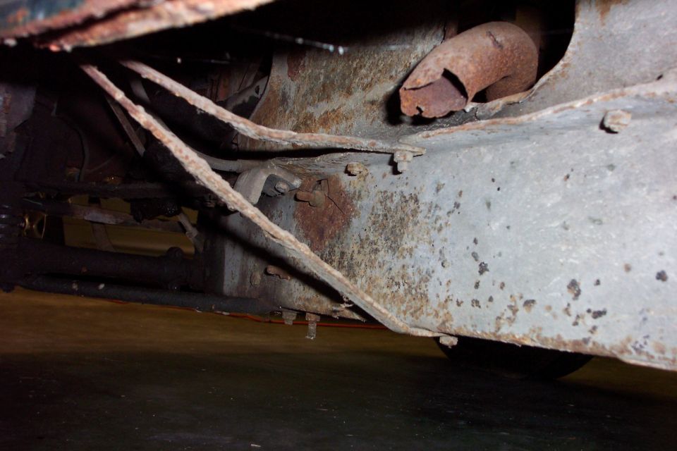 Rusty underbody floor pan, sill and exhaust stub viewed from beneath a vintage car