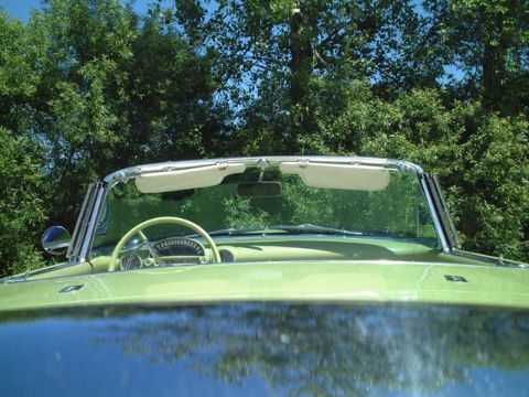 1956 Ford Thunderbird - The dashboard and steering wheel of a 1956 Ford Thunderbird convertible are visible through the windshield.