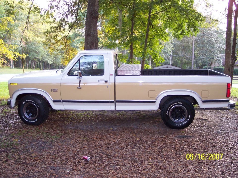 Side view of tan and white Ford F-150 pickup parked among trees