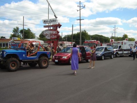 1992 Ford Bronco - A blue Jeep CJ-7 is parked in front of a shopping center with several other vehicles and emergency services present.