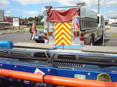 1992 Ford Bronco - A fire truck is parked on asphalt, with a police car and a person holding an American flag in the background.