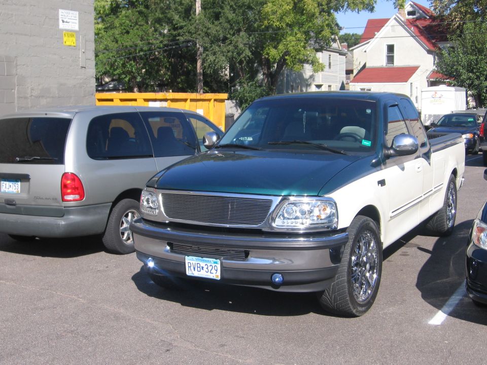 Green and white Ford F-150 pickup truck parked next to a silver minivan