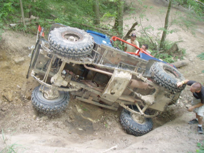 Blue off-road vehicle on its side on a dirt hill with people around it