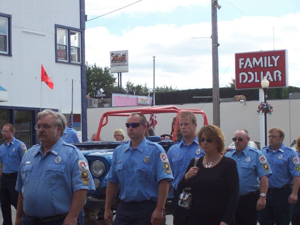 Group of people in blue uniforms walking past a blue off-road vehicle with a red roll cage