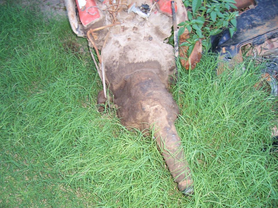 rusted car transmission and engine components lying in green grass