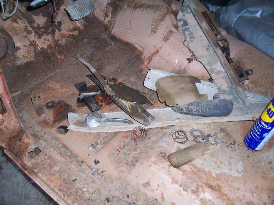 Rusted car interior floor with various disassembled parts, including a door handle and springs. A can of WD-40 is visible on the right
