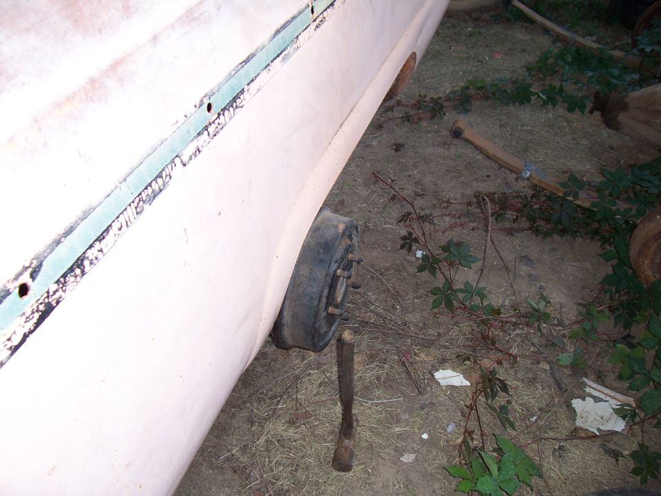 Side view of a car body with a missing wheel and a wooden block supporting it
