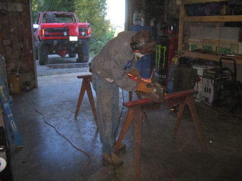 1979 Ford Bronco - A person works on metal in a garage while a modified red truck is visible outside.