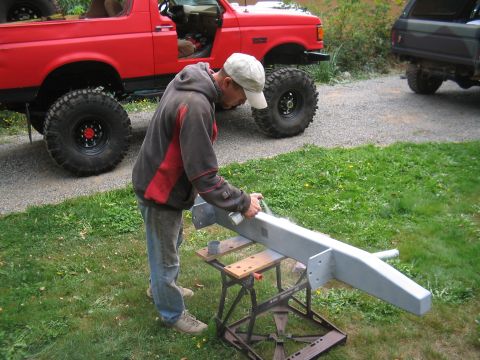 1979 Ford Bronco - A person is painting a bumper that is mounted on a portable stand outdoors.