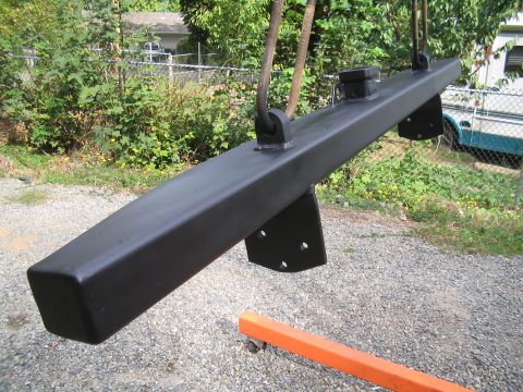1979 Ford Bronco - A heavy-duty black metal bumper is suspended by chains, ready for installation or after installation.