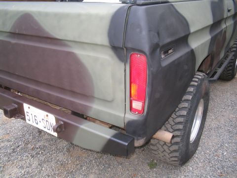 1979 Ford Bronco - Rear 3/4 close-up of a Ford pickup bed painted in flat green and brown camouflage, showing the vertical tail light, bedside dent, and a col…