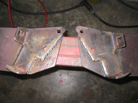 1979 Ford Bronco - Close-up of a fabricated steel bumper or mount assembly laid on a concrete shop floor, showing a pair of plate brackets freshly MIG-welded…