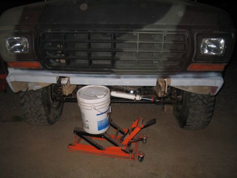 1979 Ford Bronco - Front view of a camouflage-painted truck, focusing on the bumper and grille area, with a bucket and jack positioned below.