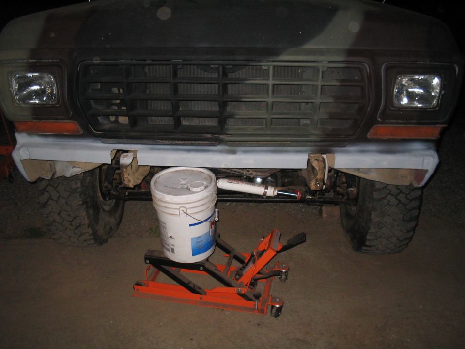 Truck front bumper and grille with camouflage paint. Bucket and jack visible underneath