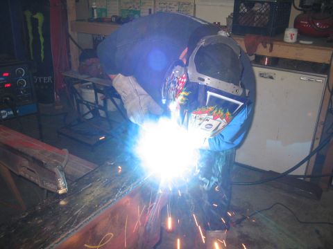 1979 Ford Bronco - A person welds a metal beam in a workshop setting, with tools and equipment visible in the background.